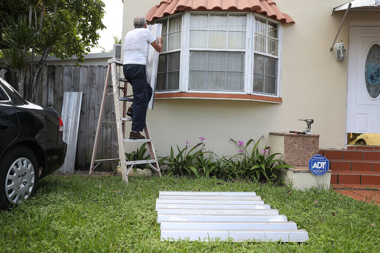 A man attaching storm shutters on to a house in Miami; links to news story