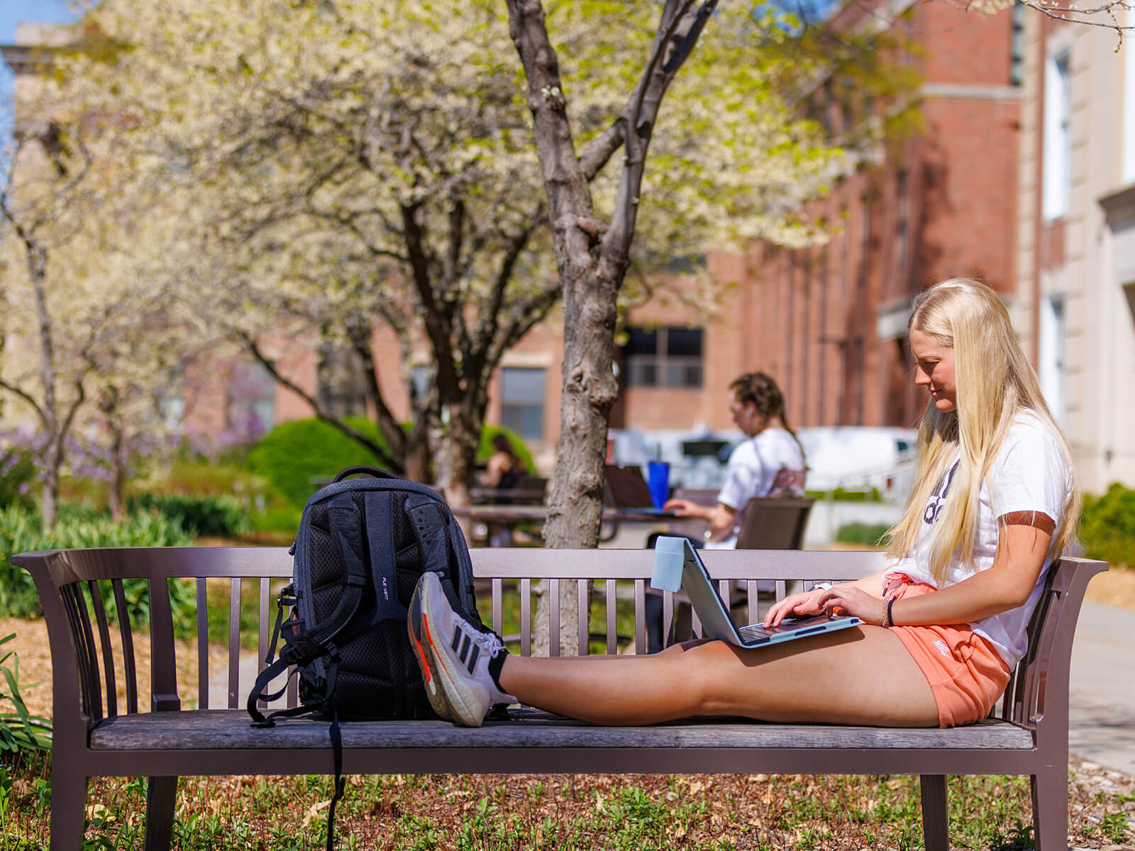 Student sitting on bench outside library with laptop