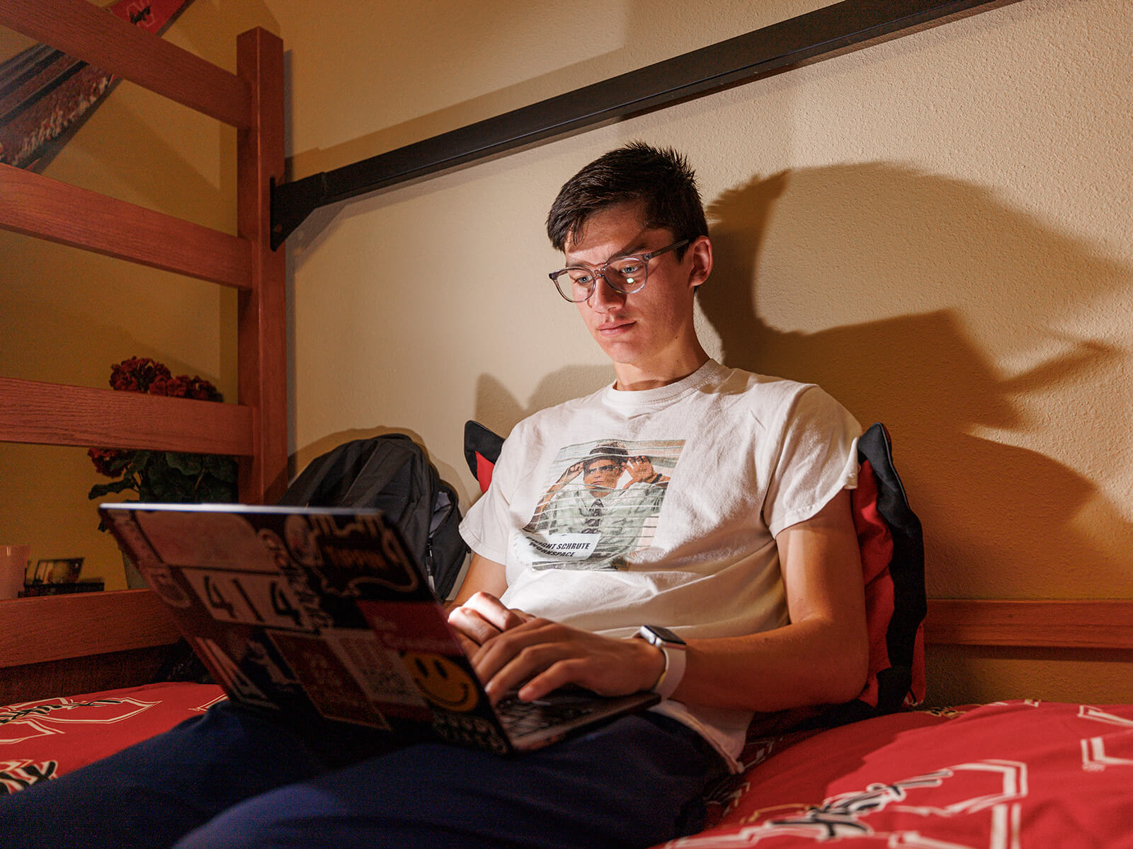 Student sitting on bed in room looking at laptop