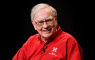 Nebraska alumnus Warren Buffett smiles while wearing a red College of Business shirt.