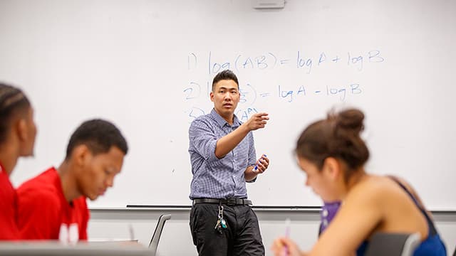 A Graduate Teaching Assistant stands in front of a whiteboard with calculus equations and leads class.