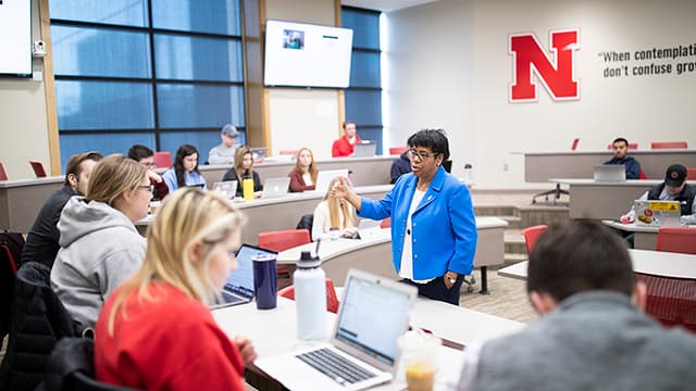 A Nebraska professor teaches a course to students sitting at tables in a College of Business classroom.