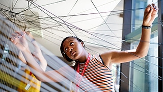A student uses string to design in the atrium of the college.