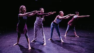 Four students perform a dance recital on a darkened stage.