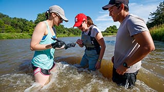 Professor and two students look over a sand sample while standing in the Niobrara River.