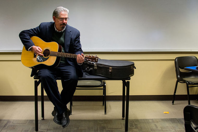 Buhler sits at the front of class with an acoustic guitar; links to news story
