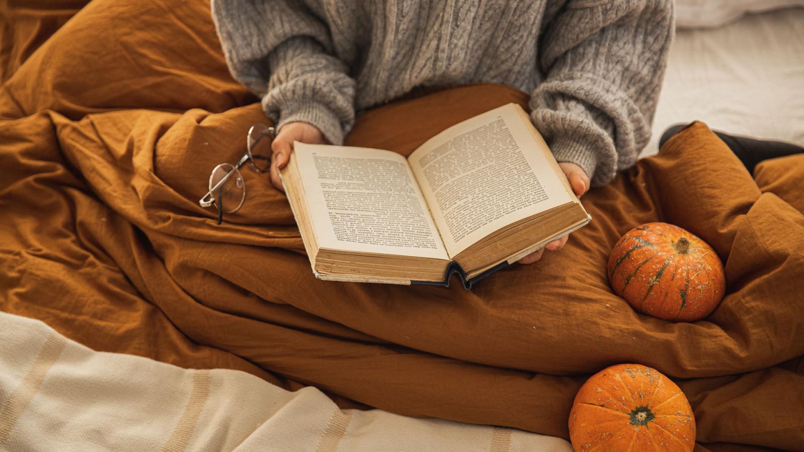 Person reading a book with a blanket and pumpkins