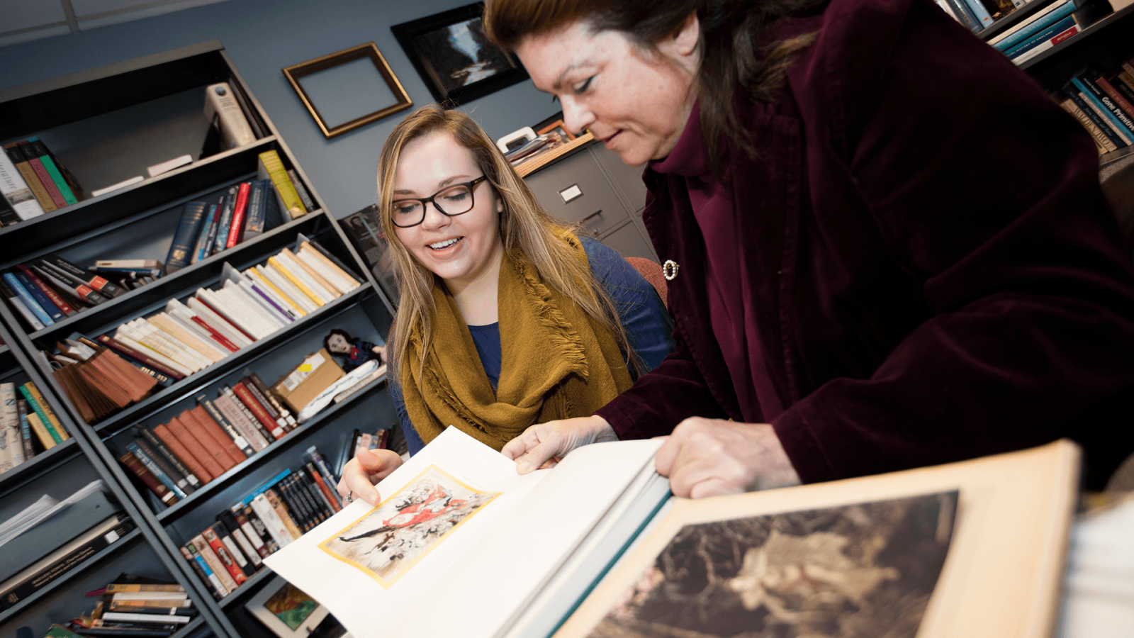 Professor Laura White shows student Amzie Dunekacke an illustrated book from the nineteenth century
