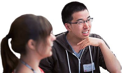 Two students are smiling while engaged in conversation. Foreground student is out of focus. Background student is in focus.
