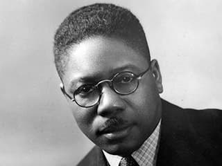 Black and white portrait of Aaron Douglas wearing a coat and tie..
