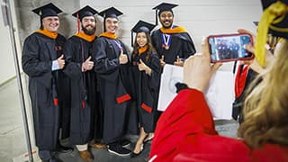 A group of five smiling graduates pose for a photo in Pinnacle Bank Arena.