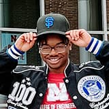 Portrait of Andre Tharp III smiling with his hands raised to the brim of his baseball cap.