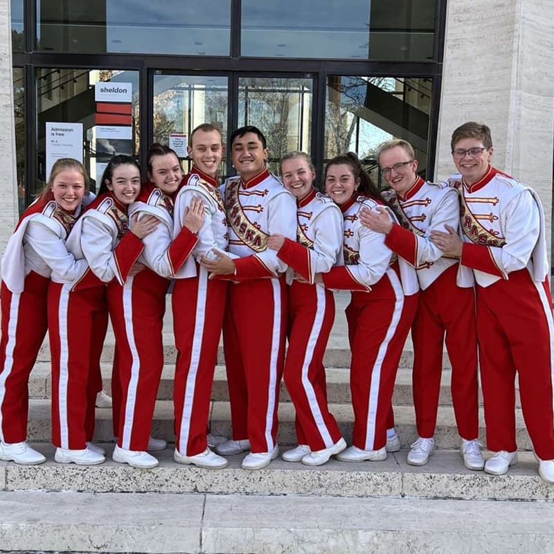 Members of the Cornhusker Marching Band, dressed in uniform, pose in front of the doors at the Sheldon Museum of Art.