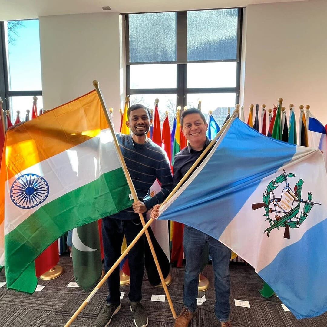 Two smiling students hold large Indian and Guatemalan flags on flag poles..