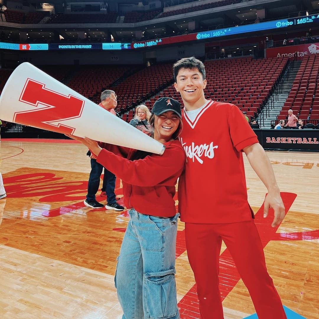 Two Huskers, one carrying a megaphone, stand on the floor of Pinnacle Bank Arena at the basketball game.