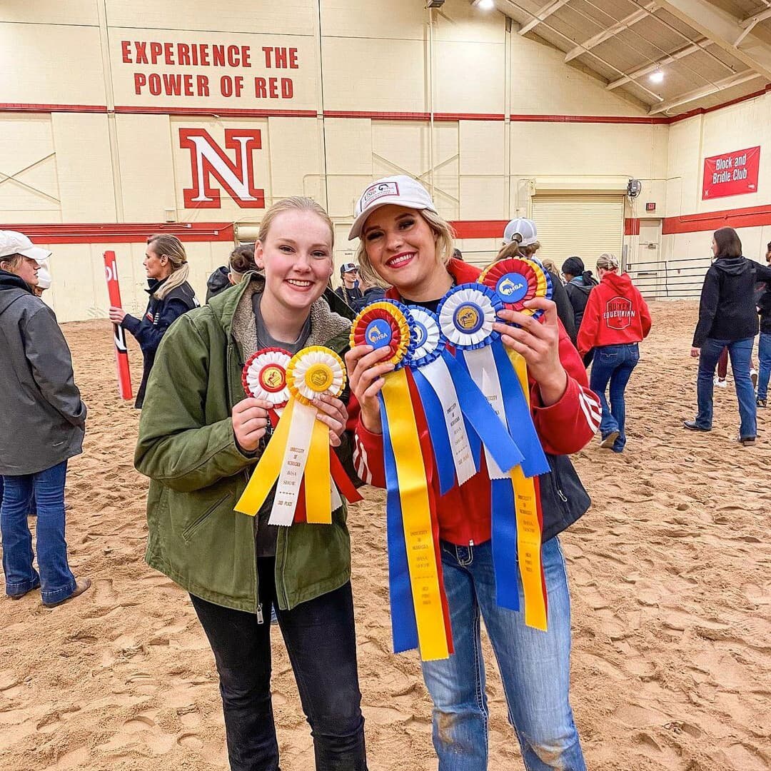 Two smiling students hold up multiple ribbons won by the Husker Equestrian team.