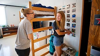 Husker student smiles at her mom after finishing decorating one of her dorm room walls with photos.