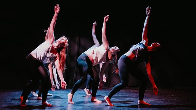 A group of dancers bend their knees and stretch their right arms above their heads during a recital.
