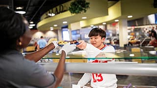 A Dining Services employee hands a student a plate of food over a glass counter.