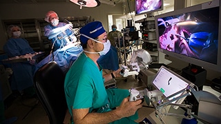 A professor operates a surgical robot while a professor adjusts the camera on the surgical subject.