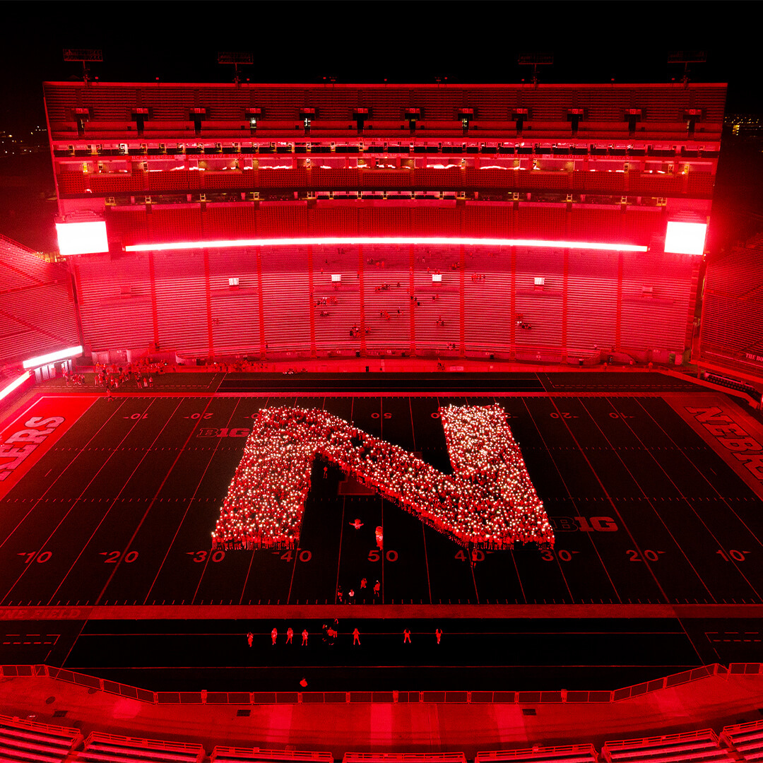 The Class of 2030 forms a glowing red 'N' on the field of Memorial Stadium at night.