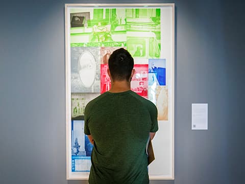 Man in a green shirt admiring a colorful collage artwork in a gallery setting.