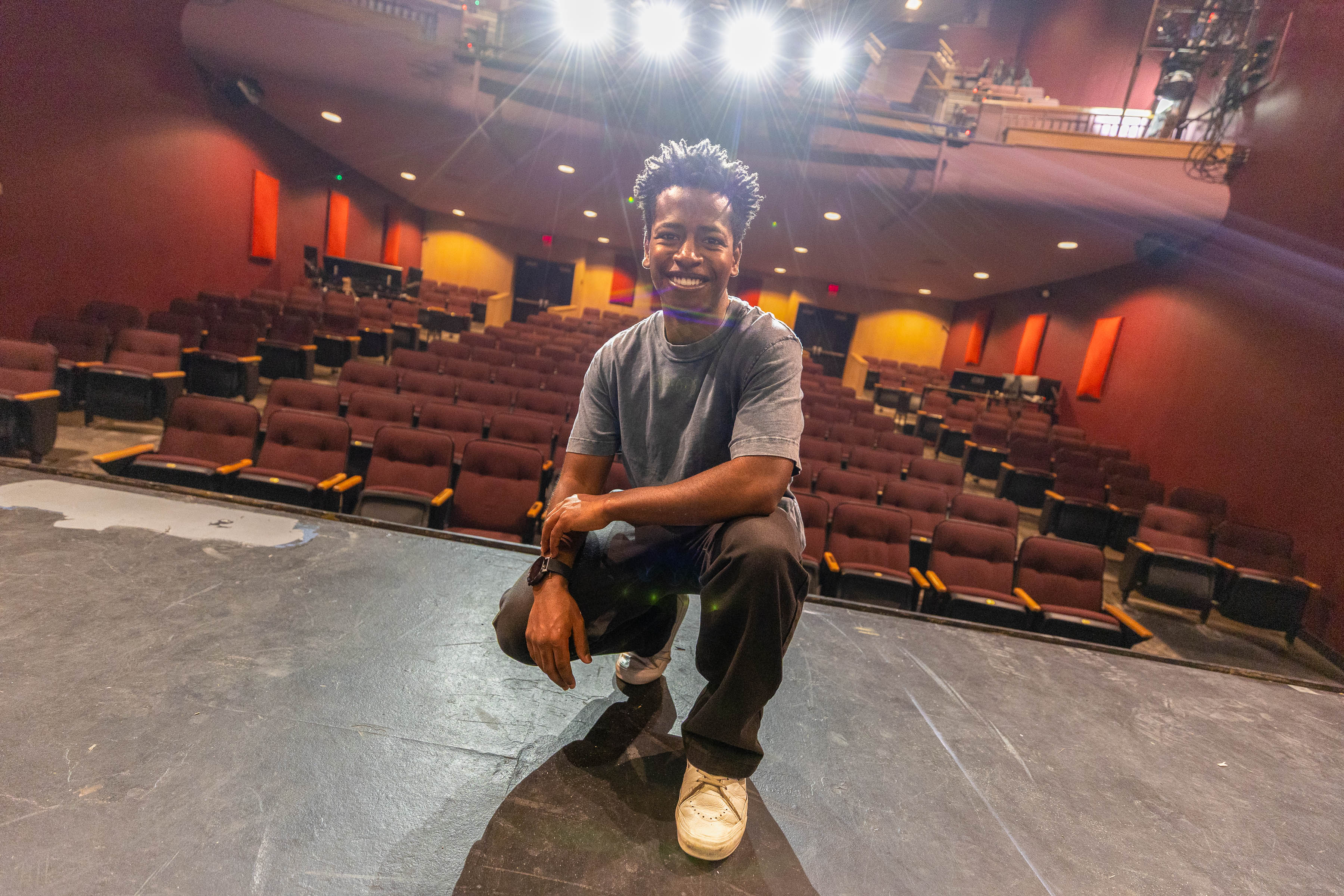 Melkie Sherman squats at the front of the Howell Theatre stage, with the theater's seats in the background. 