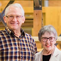 Smiling older couple standing indoors near wooden beams.