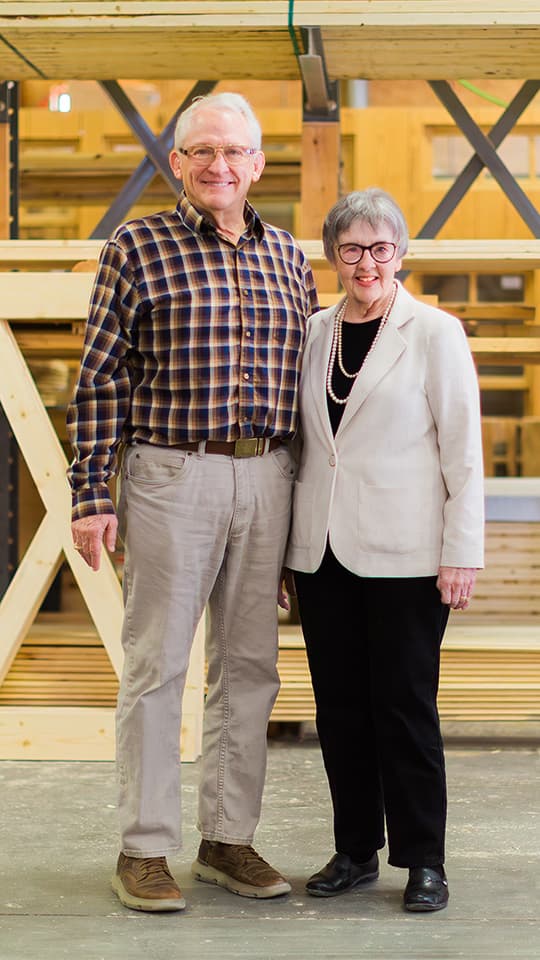 Smiling older couple standing indoors near wooden beams.