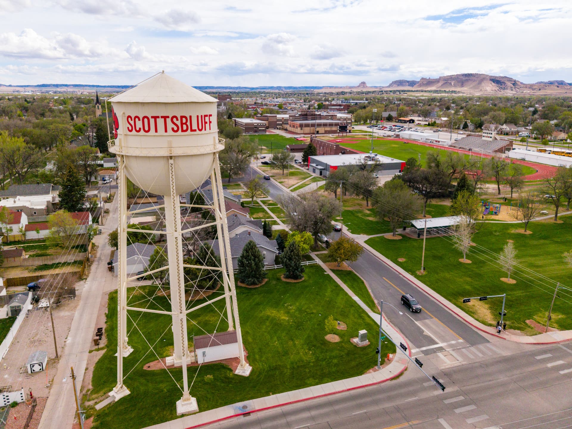 Scottsbluff water tower overlooking a town with roads, trees, buildings, and a stadium.