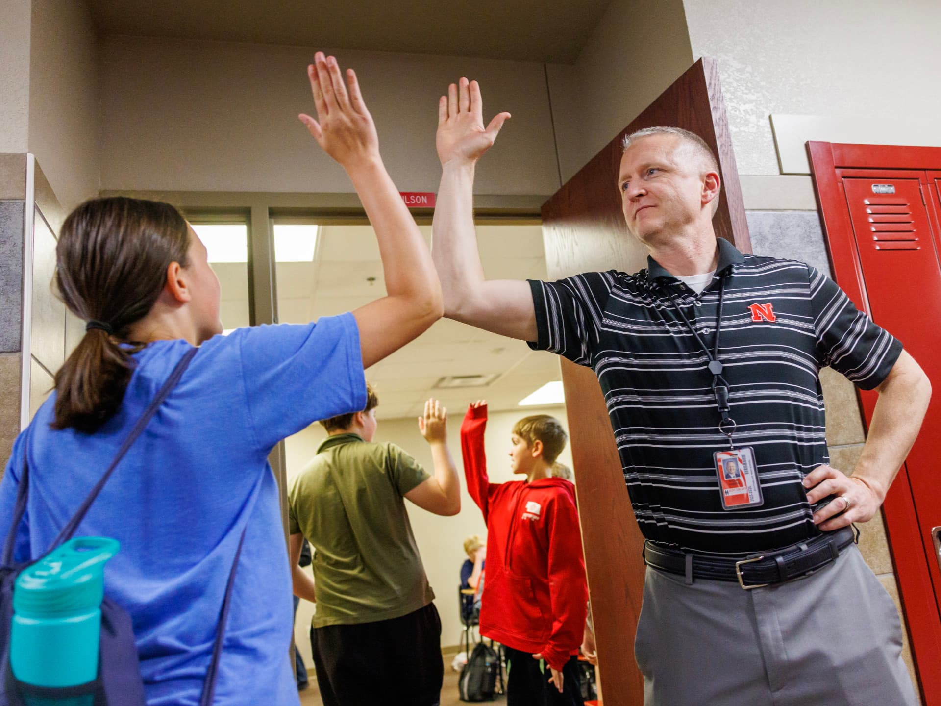 A student and teacher exchange high-fives near school lockers.