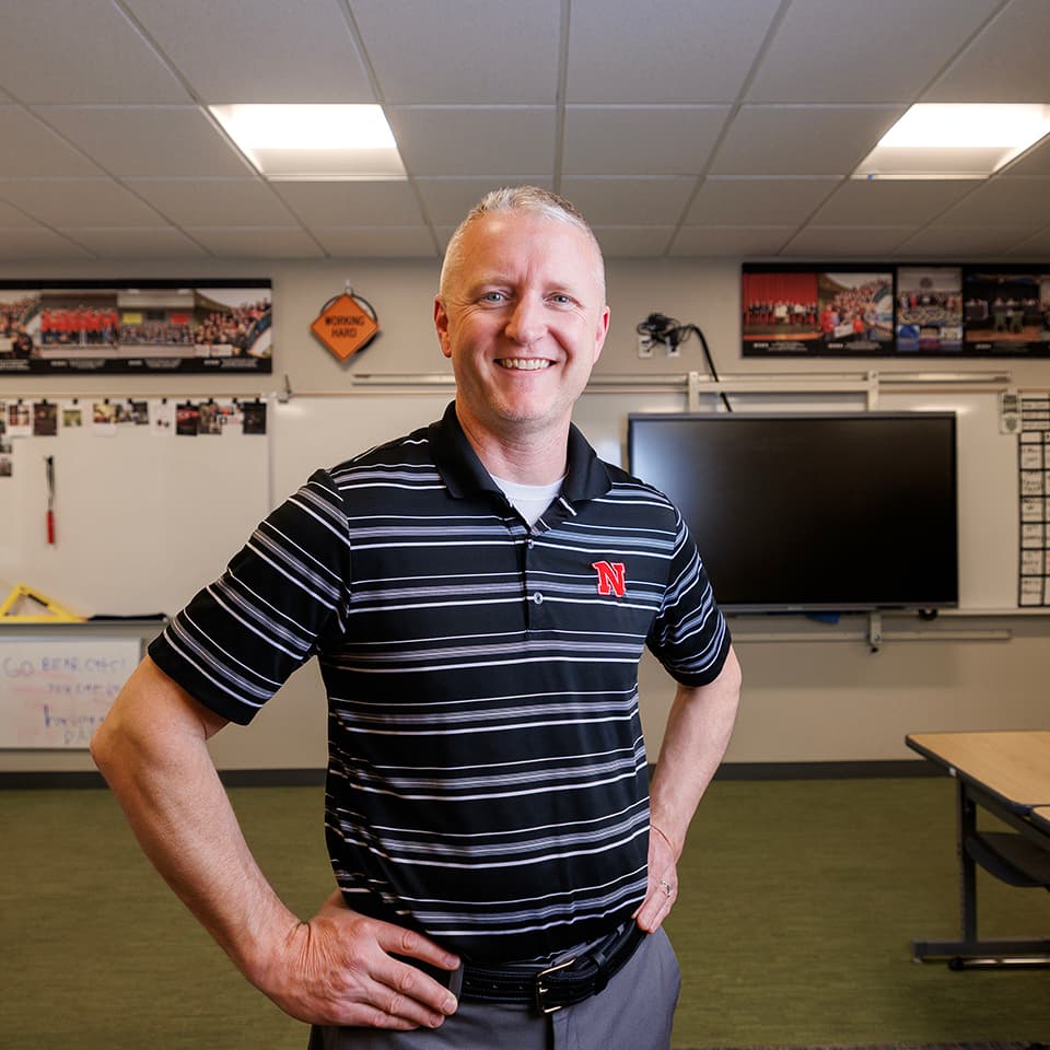 Shelby Aaberg smiles and stands with his hands on his hips in an empty classroom.