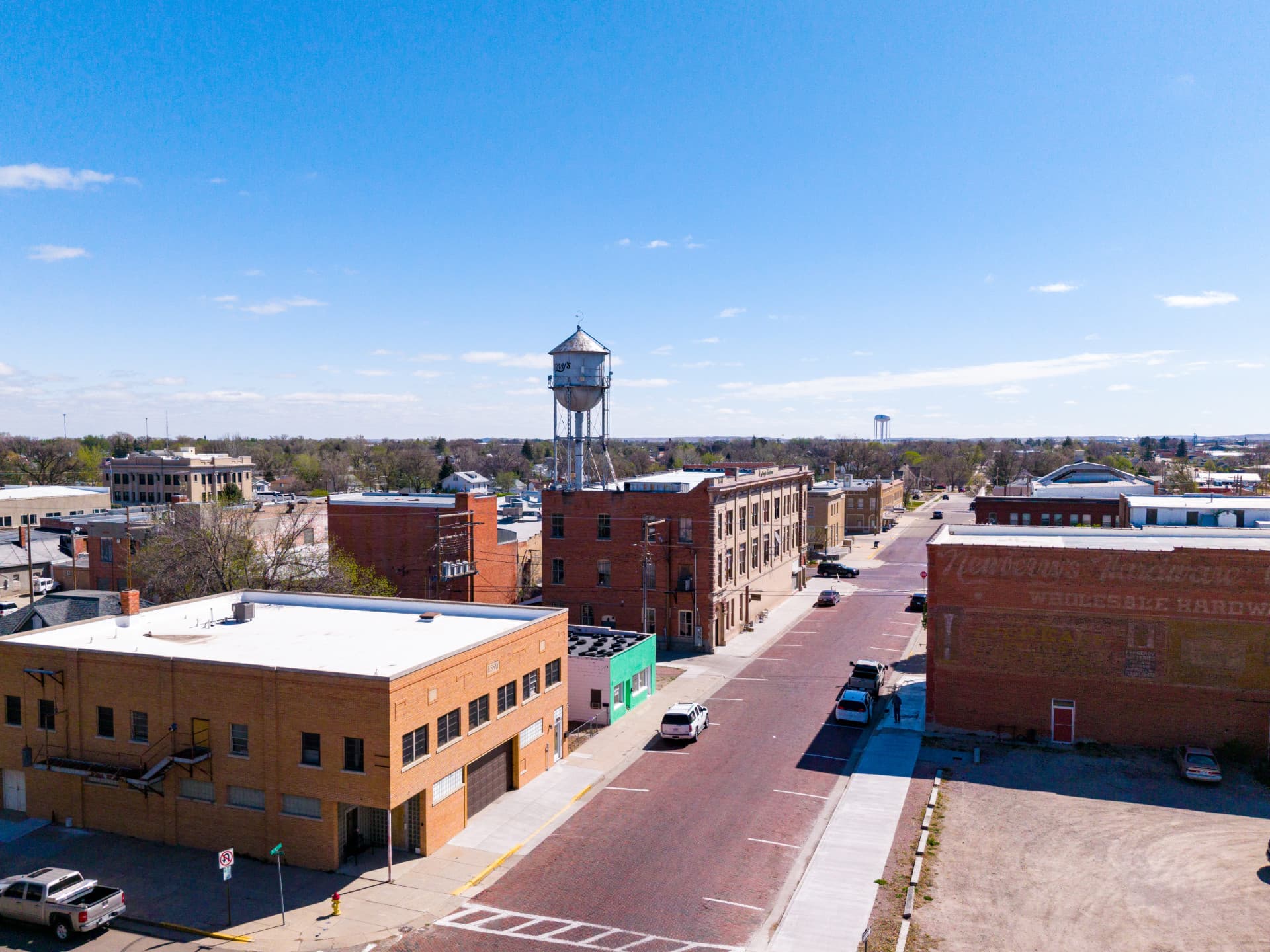 Brick street with industrial buildings, a water tower, parked cars, and a clear blue sky.