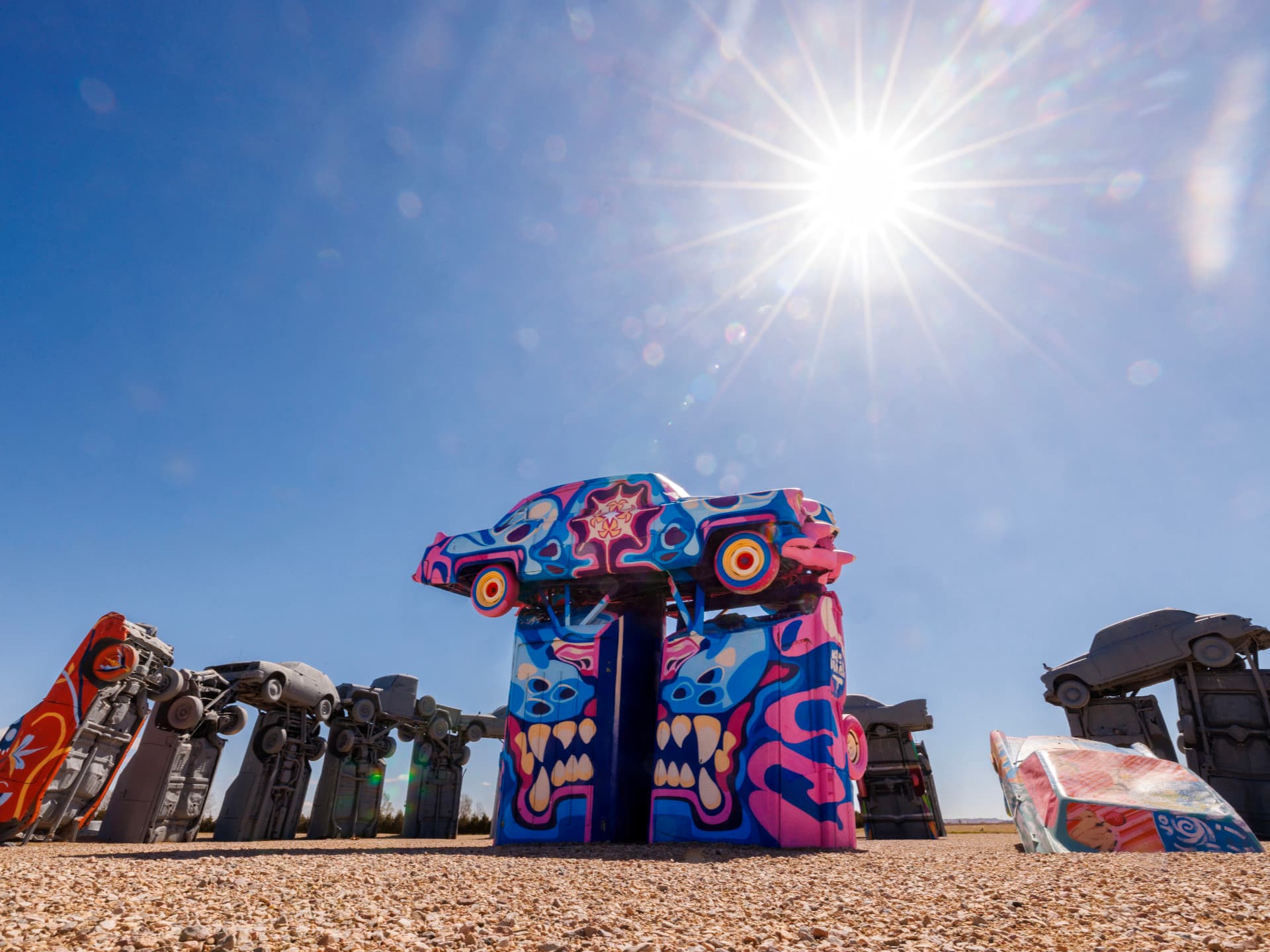 Colorful painted cars of Carhenge stacked upright under a bright sun in a desert-like setting.