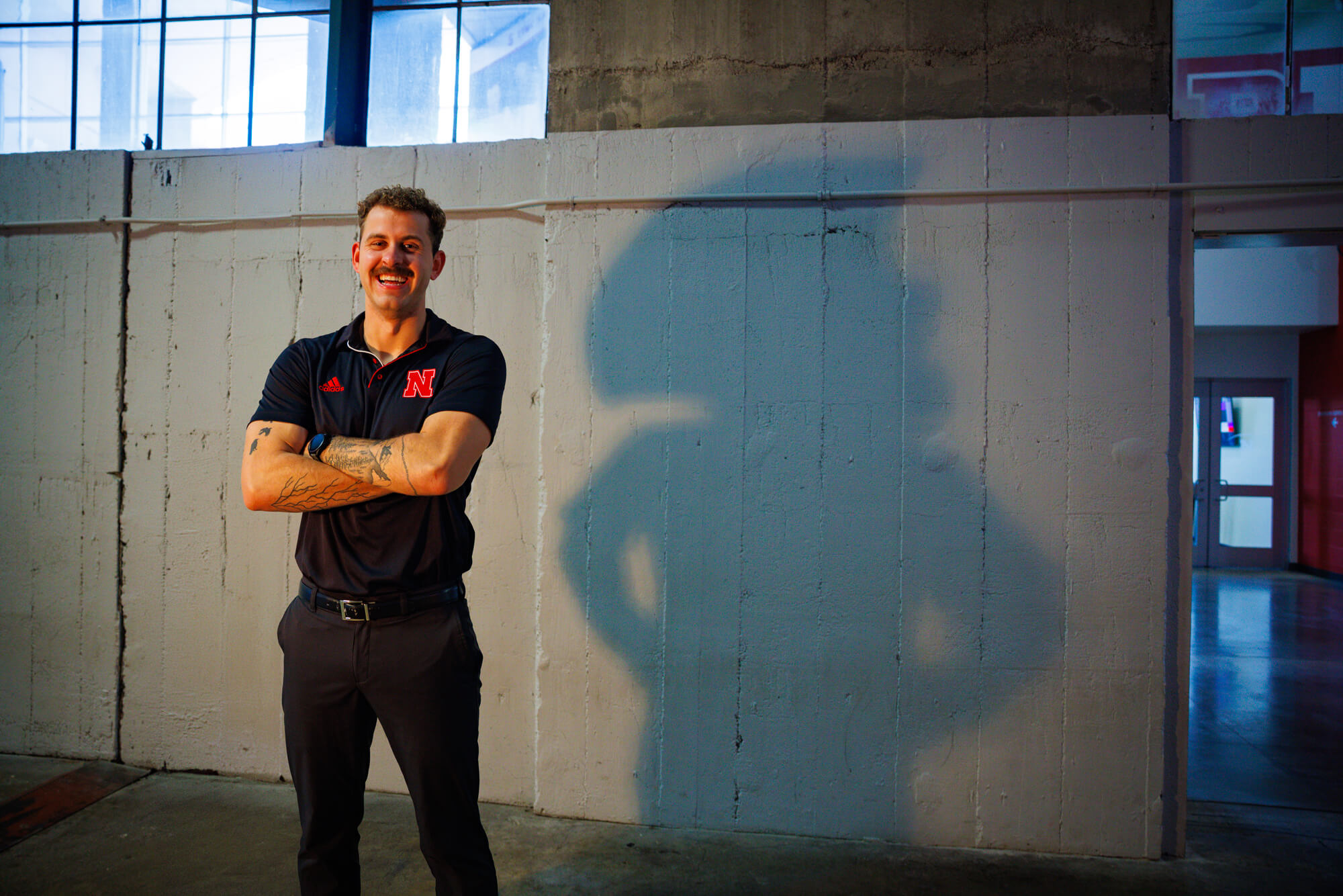 Connor smile for a photo in Memorial Stadium. On the wall behind him is the silhouette of Herbie Husker with his hands on his hips