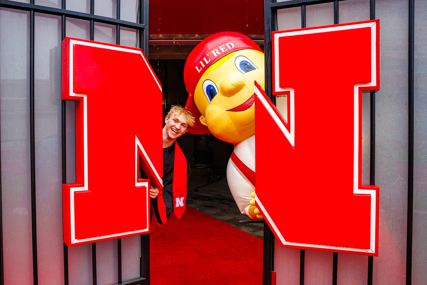 Aidan and Lil' Red smile behind large red "N" gate that leads into the Memorial Stadium tunnel