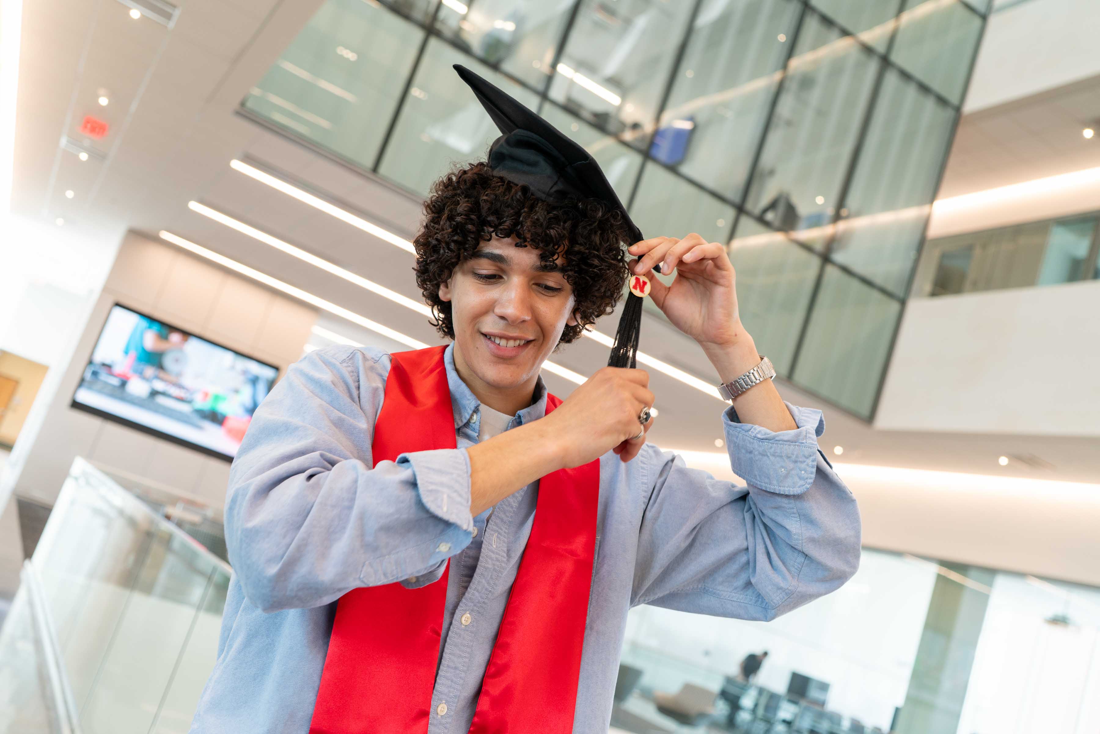 Graduation cap adjustment in a modern building, bright lighting and red academic stole.