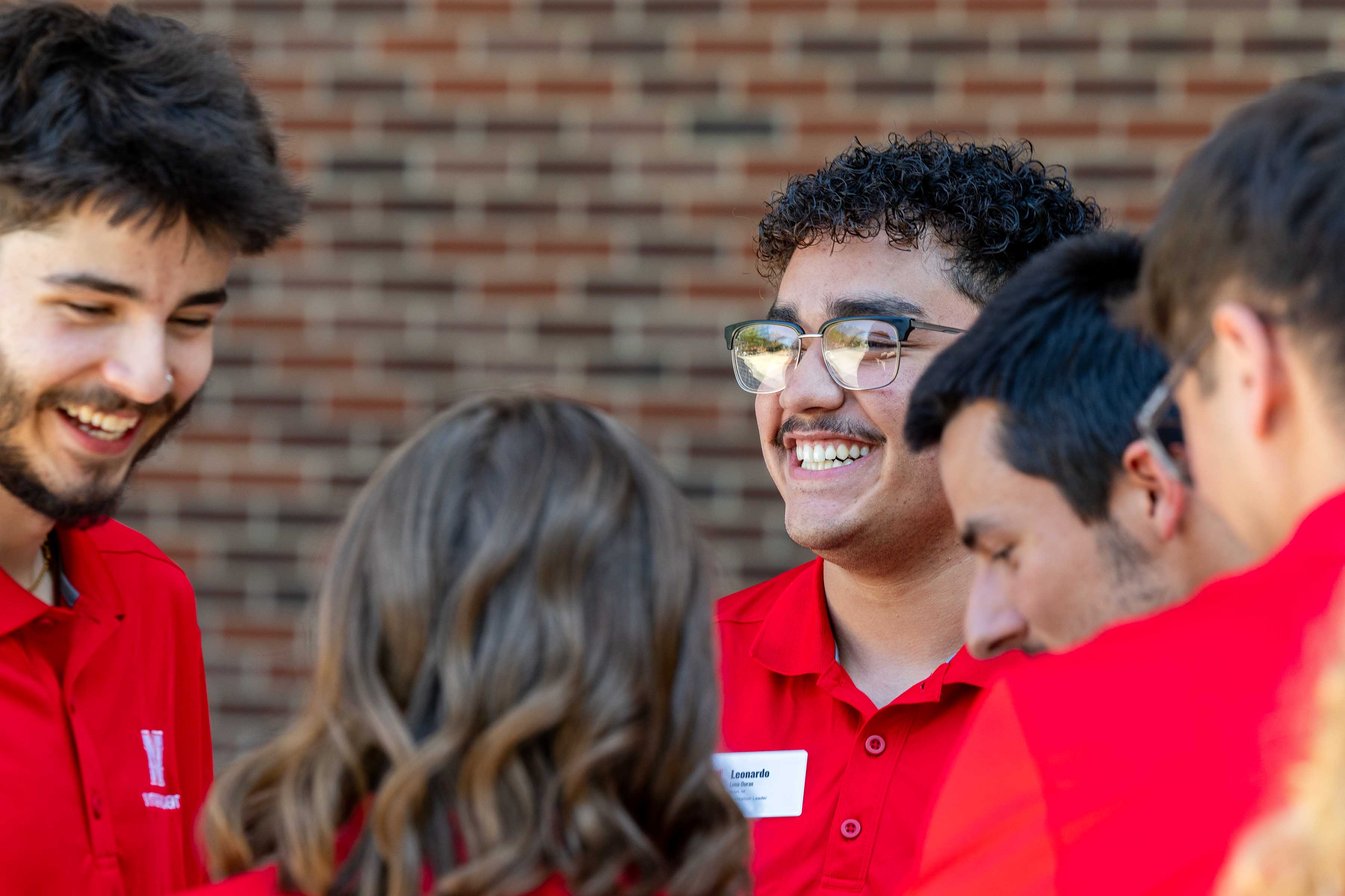 Group of people in red shirts standing together outdoors near a brick wall.