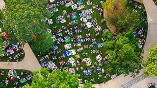 Aerial view of people gathered on colorful blankets in a greenspace surrounded by trees and pathways.