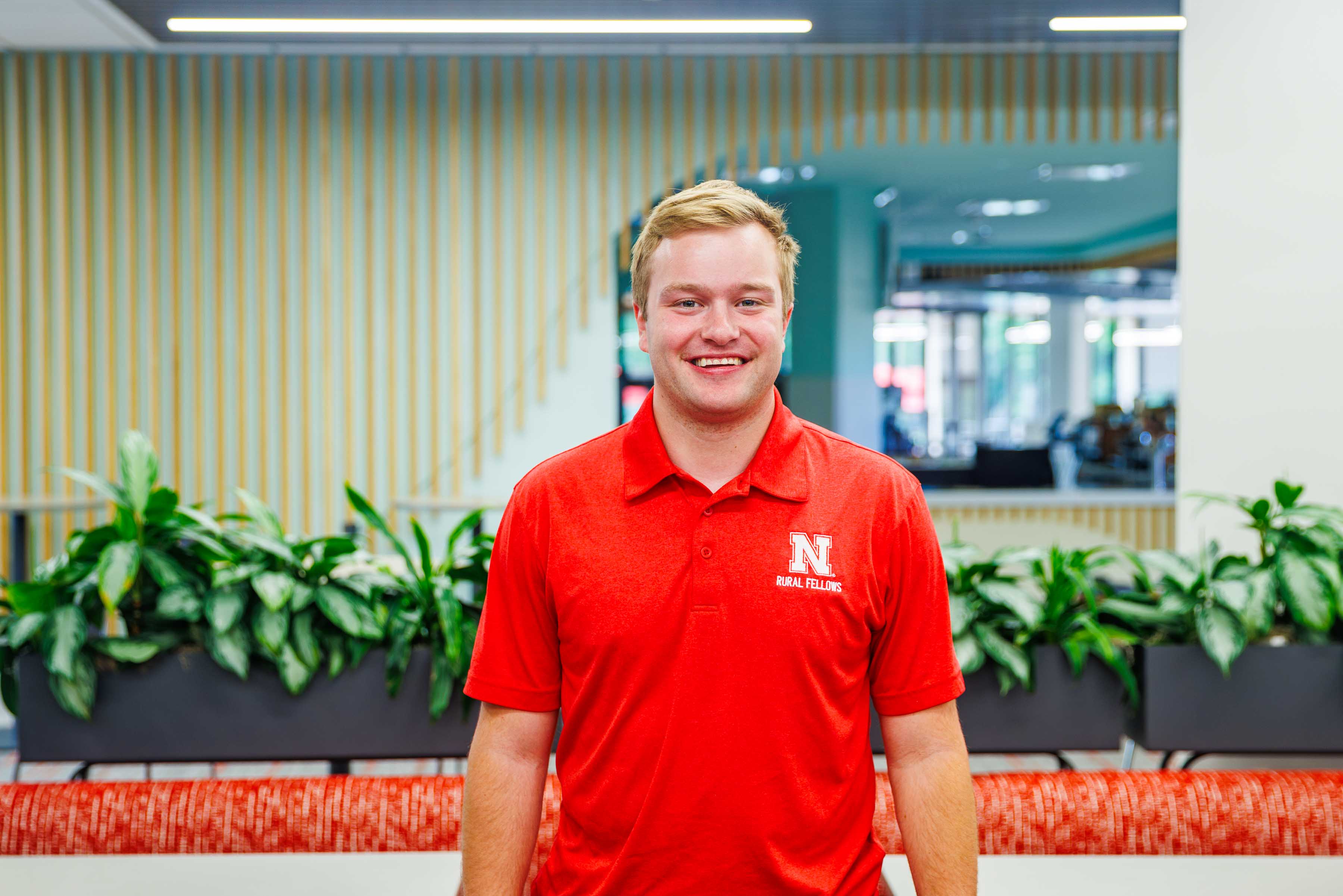 Person in a red polo shirt standing in a modern space with indoor plants and striped walls.