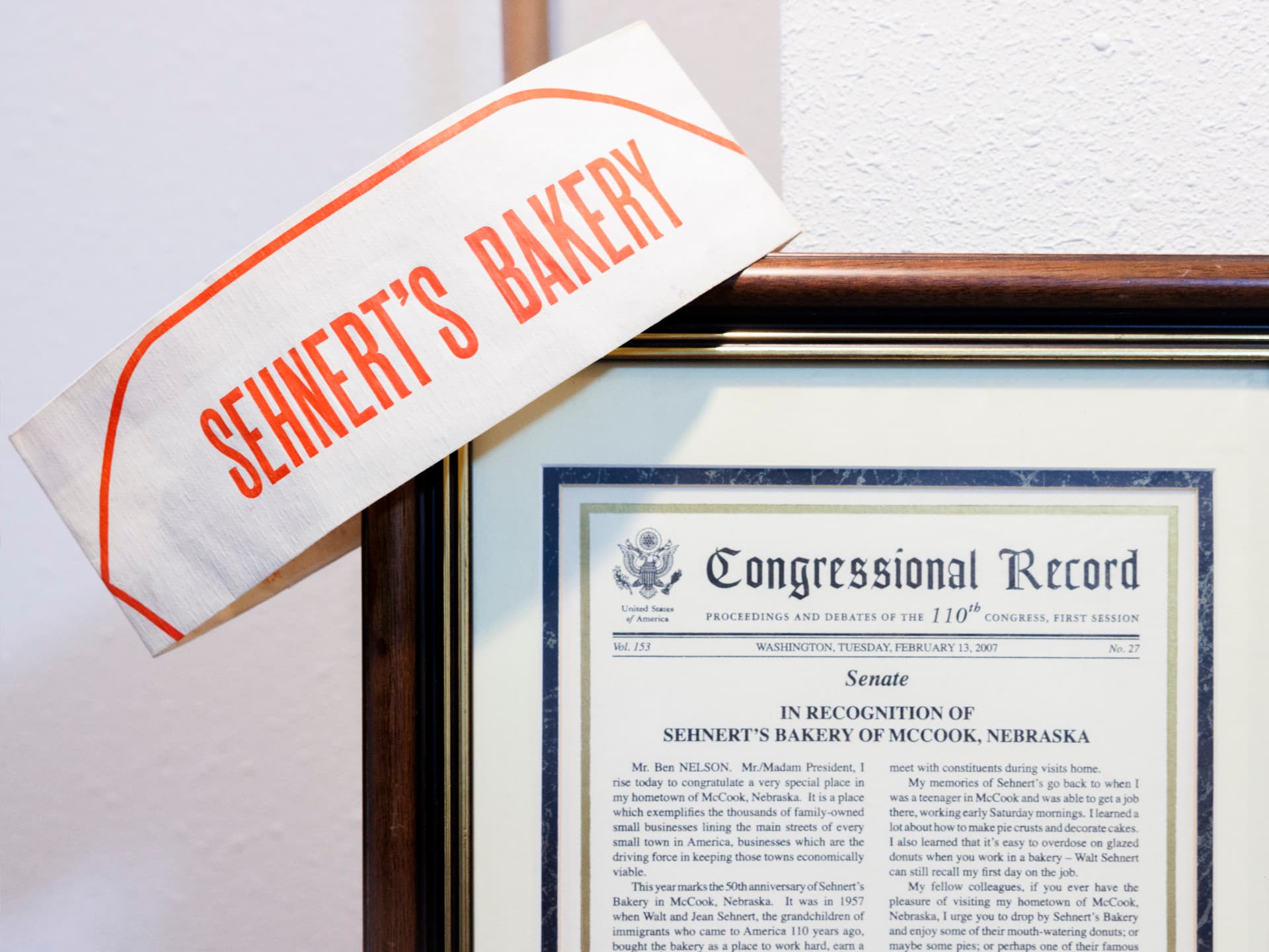 Sehnert's Bakery white paper hat next to a framed Congressional Record document on a wall.