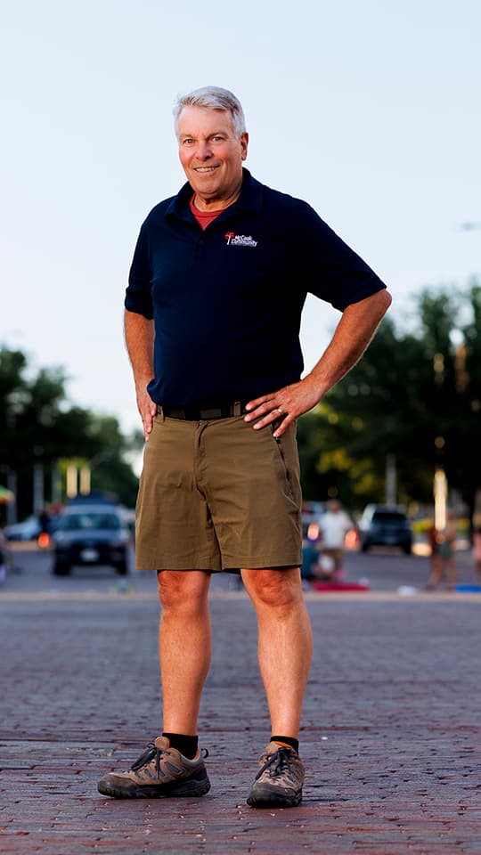 Man standing confidently outdoors on a brick road, wearing a navy shirt, khaki shorts, and sneakers.