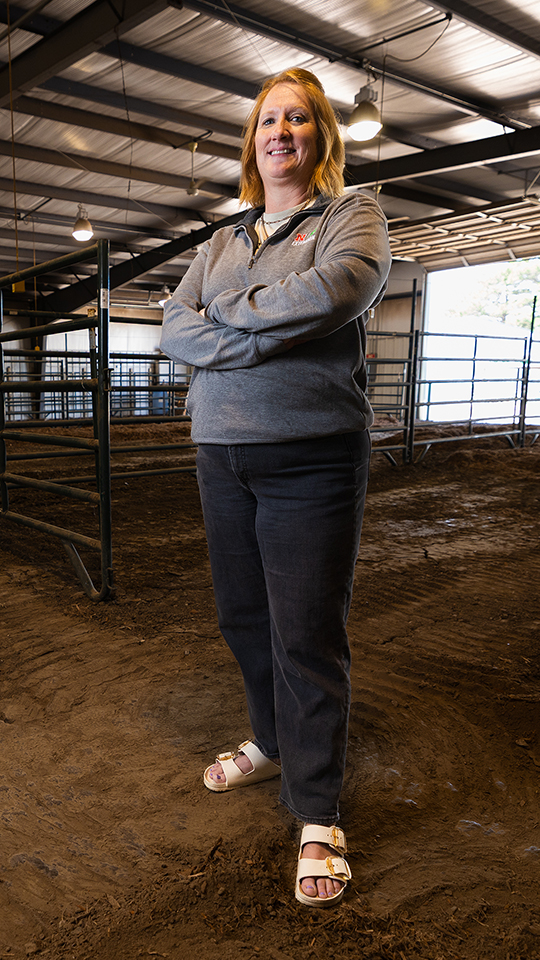 Tanya Crawford stands confidently in an indoor barn, wearing casual attire and sandals.