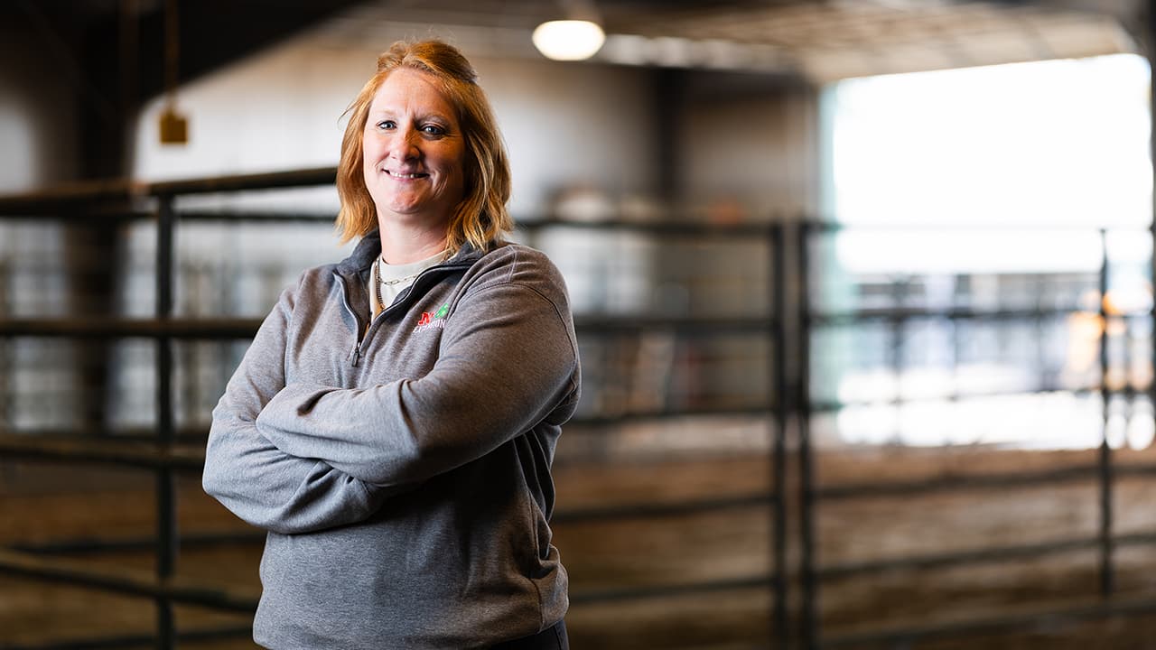 Tanya Crawford in a gray sweater stands confidently in a well-lit barn with metal fences.