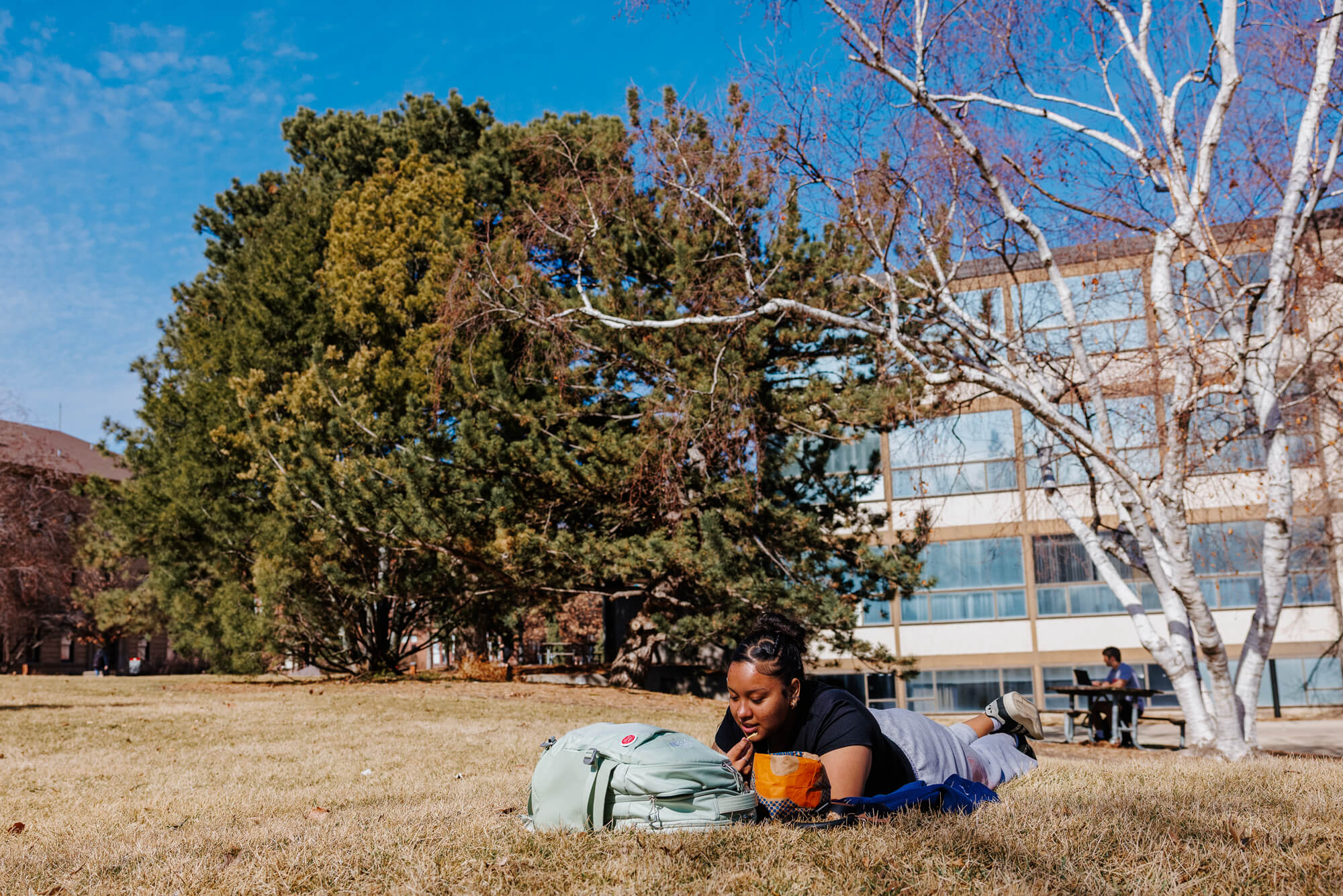A student lays in the grass and soaks up the sun on a warm February day outside the Woods Art Building