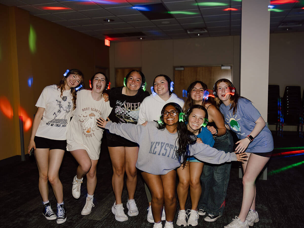 Group of smiling people wearing casual clothing and glowing headphones in a dimly lit indoor setting.