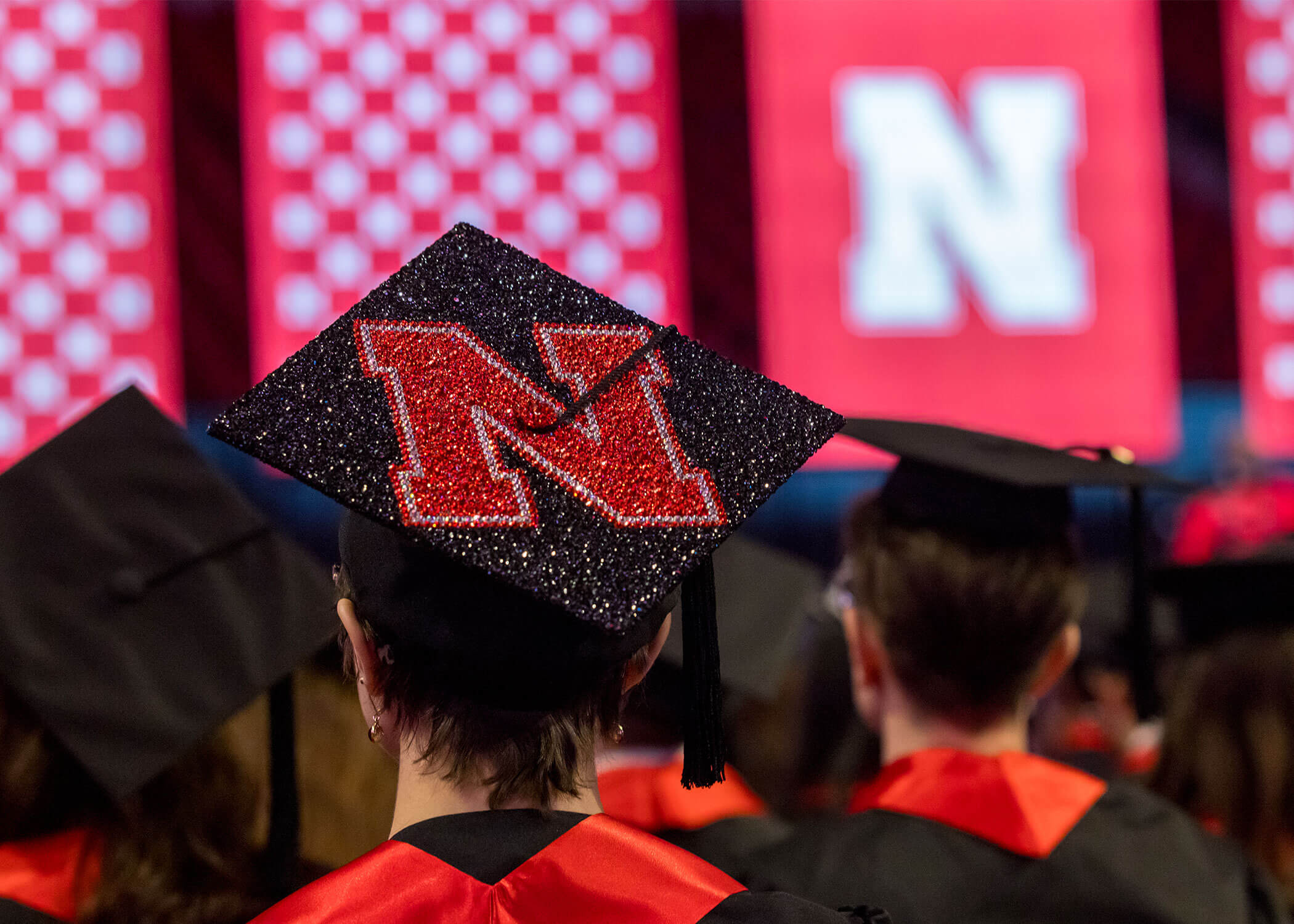 Graduation cap with a red glittery "N" in an auditorium with bright red banners.