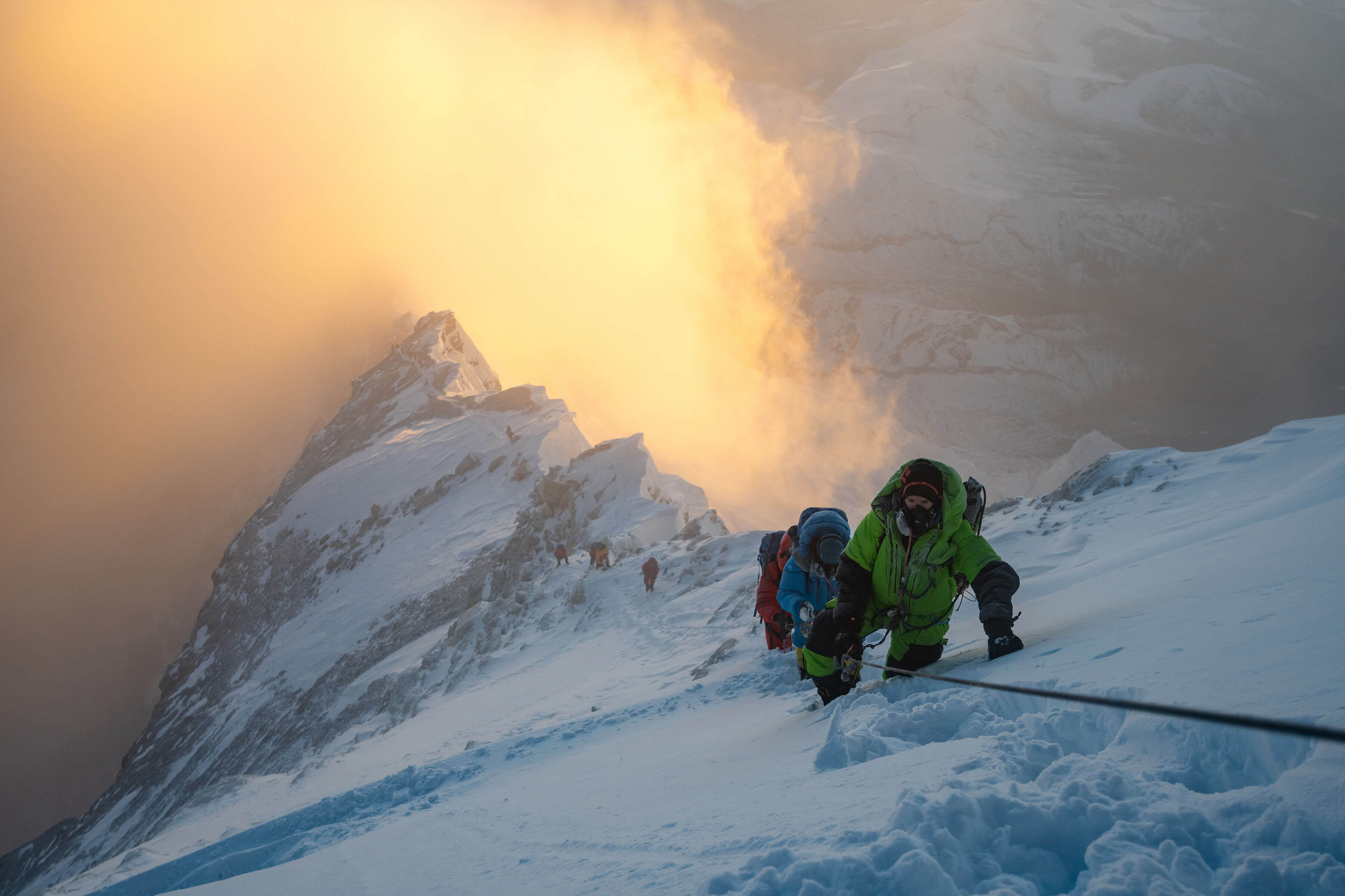 Climbers ascend a snowy Mt. Everest as the sun shines on the peaks below them
