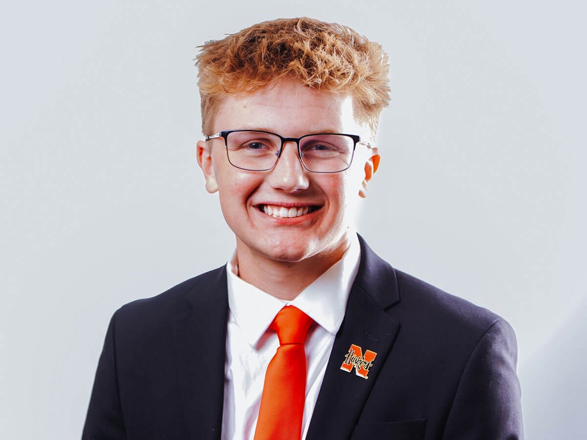 Nick Stefanik poses for his ASUN headshot in a red tie and Nebraska pin