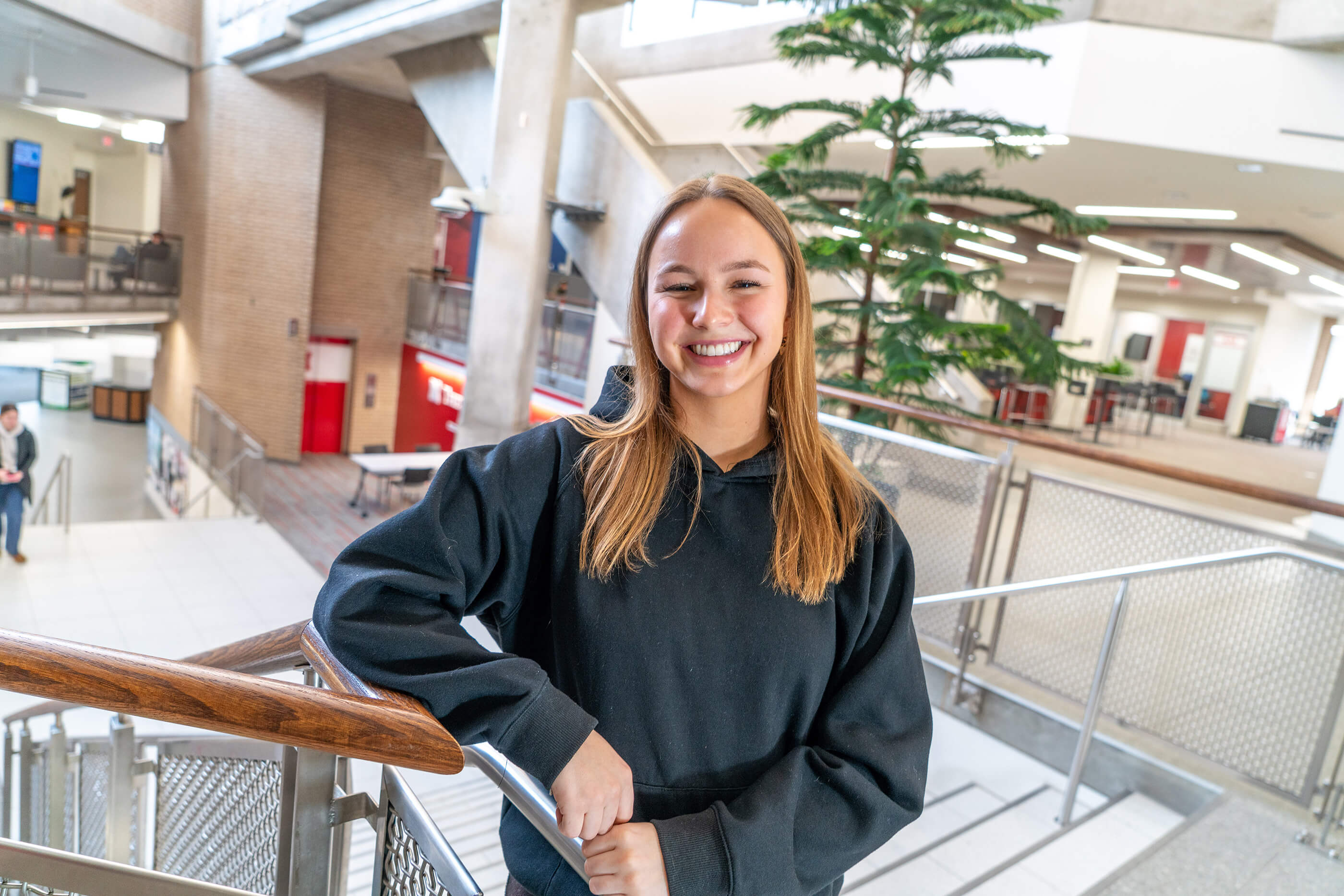 Student in black sweatshirt standing by railing in East Campus Union